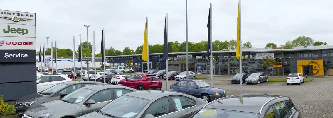 Autohaus Peter in G&ouml;ttingen mit gro&szlig;er Fahrzeugausstellung, sichtbaren Markenlogos von Jeep, Chrysler, Dodge und Opel sowie zahlreichen Flaggen.
