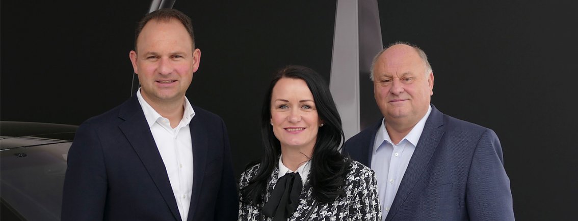 Die Gesch&auml;ftsf&uuml;hrung der Peter Autozentrum Anhalt GmbH: Andreas Peter (links), Christina Dost (Mitte) und Helmut Peter (rechts) stehen nebeneinander in Businesskleidung und l&auml;cheln in die Kamera; dunkler Hintergrund.