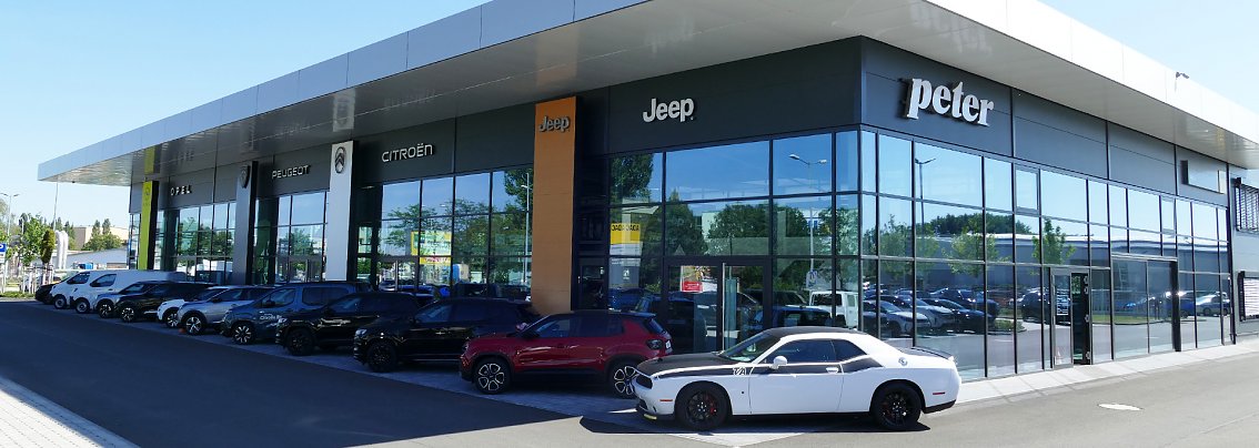 Modernes Mehrmarken-Autohaus Peter in Erfurt mit gro&szlig;en Glasfassaden, Logos von Jeep, Citro&euml;n und Peugeot sichtbar, viele Neuwagen vor dem Geb&auml;ude, sonniger Tag.