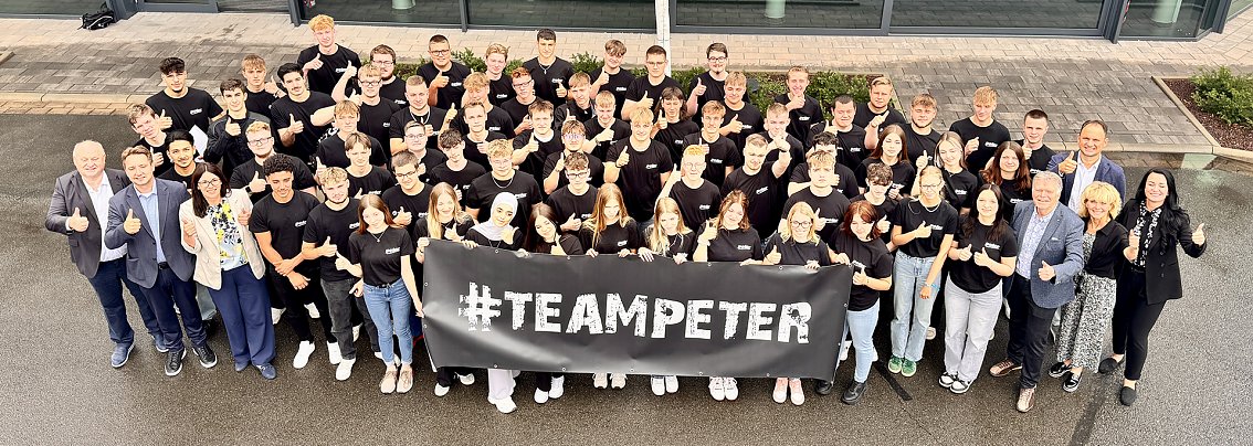 Gruppenfoto der 63 neuen Auszubildenden der Autohaus-Peter-Gruppe vor dem Mercedes-Benz-Autohaus in Nordhausen. Alle tragen schwarze #TeamPeter-T-Shirts und halten einen Banner mit dem Schriftzug �#TEAMPETER�. Gesch&auml;ftsf&uuml;hrung und Ausbildungsleitung stehen am Rand, alle l&auml;cheln und zeigen Daumen hoch.