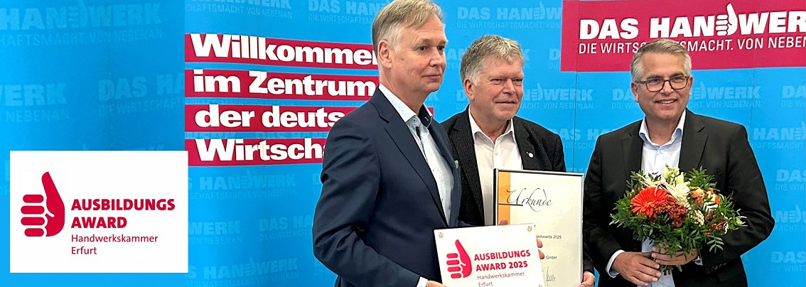 Drei M&auml;nner stehen vor einer blauen Wand mit dem Schriftzug Das Handwerk � Die Wirtschaftsmacht von nebenan. Einer h&auml;lt eine Urkunde, ein anderer eine Blumenstrau&szlig;, der dritte das Schild Ausbildungsaward 2025 Handwerkskammer Erfurt. Das Bild zeigt die &Uuml;bergabe des Ausbildungsawards an die Autohaus Peter Gruppe.
