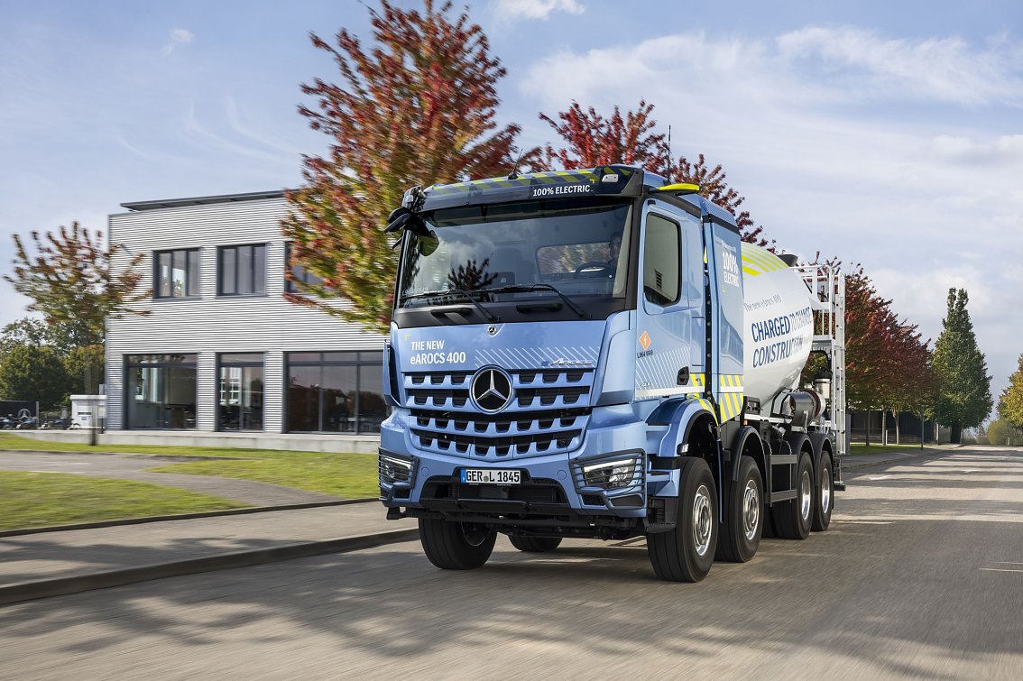 Elektrischer Betonmischer Mercedes-Benz eArocs 400 steht vor einem modernen Firmengeb&auml;ude mit B&auml;umen im Hintergrund