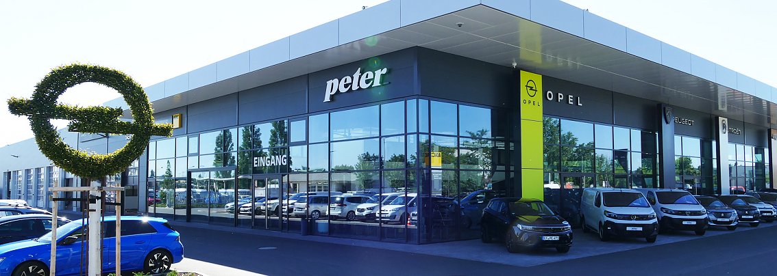 Modernes Opel Autohaus Peter in Erfurt mit gro&szlig;er Glasfassade; davor Autos und ein Baum, der in Form des Opel-Logos gestutzt ist.