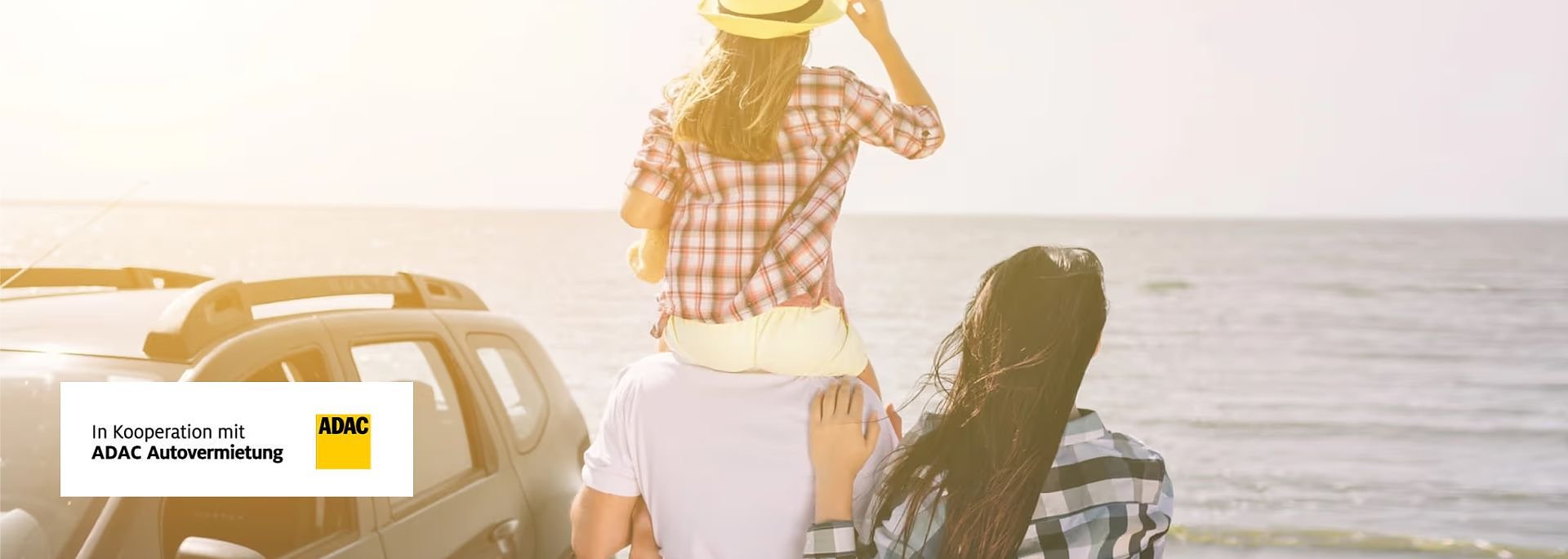 Familie am Strand: Mann tr&auml;gt Kind auf den Schultern, Frau steht daneben, alle blicken aufs Meer; links unten ADAC-Logo mit Text In Kooperation mit ADAC Autovermietung.