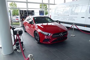 Roter Mercedes-Benz im Autohaus-Ausstellungsraum in Heiligenstadt. Das Fahrzeug ist mit roten Absperrseilen umrandet. Im Hintergrund ein großer weißer Transporter und Farbmuster. Große Fensterfronten lassen viel Tageslicht herein.