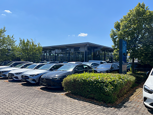 Au&szlig;enansicht des Mercedes-Benz Autohauses Peter in Dessau. Es stehen viele schwarze, wei&szlig;e und silberne Mercedes-Benz Fahrzeuge in einer Reihe auf dem Parkplatz. Im Hintergrund modernes Glasgeb&auml;ude mit gro&szlig;en Fenstern, B&auml;umen und blauem Himmel.