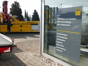 Schild an einer Glasfassade des ADAC Mobilitätspartners Peter in Nordhausen. Das Schild listet angebotene Leistungen auf, wie Pannen- und Unfallhilfe, Autovermietung, Schadenservice sowie Partnerleistungen wie Fahrzeugreparatur, Unfallreparatur, Glas- und Reifenservice, Autovermietung und Kranservice. Im Hintergrund ein gelber ADAC-Abschleppwagen.