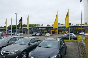 Opel-Autohaus Peter in Göttingen mit moderner Glasfassade, mehreren gelben Opel-Flaggen im Vordergrund und zahlreichen geparkten Fahrzeugen auf dem Außengelände.