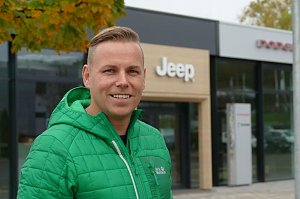 Ihr Verkaufsberater für die amerikanischen Fabrikate: Danny Kindervater mit grüner Jacke steht lächelnd vor dem Jeep-Autohaus, im Hintergrund das Eingangsportal mit Jeep-Logo.