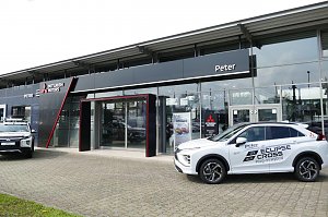 Eingangsbereich des Peter-Mehrmarkenhauses in Göttingen mit Mitsubishi-Logo, einem weißen Mitsubishi Eclipse Cross Plug-in Hybrid und einem weiteren Mitsubishi-Pickup vor dem Gebäude.
