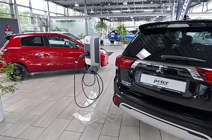Innenraum eines Autohauses mit mehreren Mitsubishi-Fahrzeugen, im Vordergrund eine Ladestation für Elektrofahrzeuge zwischen einem roten Kleinwagen und einem schwarzen SUV.