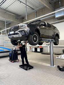 Mechaniker arbeitet unter einem angehobenen schwarzen Mercedes-Pick-up auf einer Hebebühne in der Werkstatt des Mercedes-Autohauses in Wittenberg.
