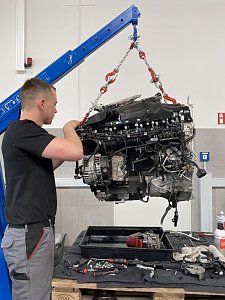Mechaniker überprüft einen mit einem Kran angehobenen Motorblock in der Mercedes-Werkstatt.
