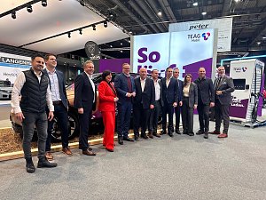 Eine große Gruppe von Männern und einer Frau posiert gemeinsam für ein Foto vor einem Stand der Firma TEAG Mobil auf der Automobilmesse Erfurt 2025. Im Hintergrund sind ein Elektroauto, ein Ladegerät und Werbebanner zu sehen.