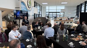 Torsten Wiesner h&auml;lt einen Vortrag mit der Pr&auml;sentation Herausforderungen der Energiewende. Teilnehmende sitzen an runden Tischen mit Kaffee und Fr&uuml;hst&uuml;cksplatten.