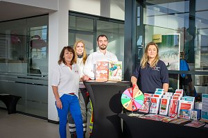 Vier Personen stehen hinter einem Infostand im �koda Autohaus. Auf dem Tisch liegen Broschüren und ein Glücksrad. Die Personen tragen Kleidung mit Logos des Deutschen Roten Kreuzes.