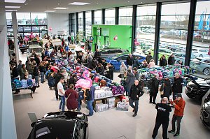 Blick von oben in den hellen Ausstellungsraum des Autohauses. Viele Besucher schauen sich an langen Tischen bunte Schulranzen an. Im Hintergrund stehen Autos, rosa Flamingos als Deko hängen von der Decke.