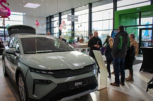 Ein neues �koda-Fahrzeug mit geöffnetem Kofferraum steht im hellen Showroom. Besucher unterhalten sich daneben, rosa Flamingo-Dekorationen hängen von der Decke.