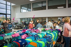 Viele Besucher stehen an Tischen voller bunter Schulranzen. Im Hintergrund ist ein schwarzes �koda-Fahrzeug ausgestellt, rosa Flamingos hängen von der Decke.