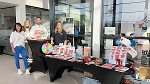 Vier Personen stehen hinter einem Infostand im �koda Autohaus. Auf dem Tisch liegen Broschüren und ein Glücksrad. Die Personen tragen Kleidung mit Logos des Deutschen Roten Kreuzes.
