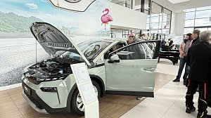 Ein helles �koda-Fahrzeug mit geöffneter Motorhaube und Fahrertür steht im Showroom. Besucher betrachten das Auto, im Hintergrund Flamingo-Dekoration.