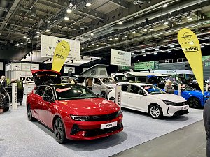 Ein roter Opel Astra und ein weißer Opel Grandland Hybrid stehen nebeneinander auf der Ausstellungsfläche, mit Opel-Fahnen und Peter-Bannern im Hintergrund.