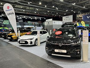 Ein schwarzer und ein weißer Suzuki stehen nebeneinander. Im Hintergrund weitere Autos verschiedener Marken unter Peter-Bannern.