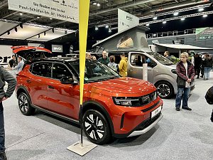 Ein roter Opel SUV im Vordergrund, dahinter ein Opel Crosscamp Camper mit geöffnetem Hochdach. Besucher stehen daneben.