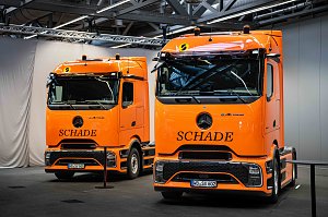 Zwei orangefarbene Mercedes-Benz eActros 600 Sattelzugmaschinen mit Schade-Logo in einer Halle.