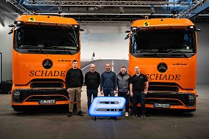 Das Team von Schade Logistic posiert mit 5 Personen vor zwei orangefarbenen Mercedes-Benz eActros-Lkw mit Schade-Logo und leuchtendem E-Symbol.