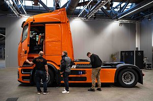 Drei M&auml;nner betrachten die Seite eines orangefarbenen Mercedes-Benz eActros in einer Halle.
