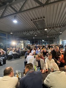 Gro&szlig;er Saal im Autohaus, viele Menschen sitzen dicht gedr&auml;ngt an langen Tischen und h&ouml;ren der CDU-Veranstaltung zu.