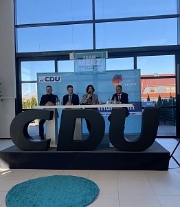 Frontalaufnahme der Podiumsdiskussion mit vier Personen, mittig Colette Boos-John. Vor ihnen große CDU-Buchstaben, im Hintergrund Team Merz 2025-Plakat.