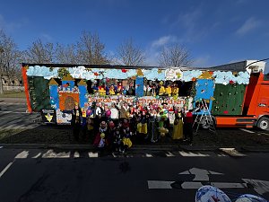 Große Gruppe verkleideter Menschen posiert vor und auf einem bunt gestalteten Karnevalswagen mit Märchenmotiven, viele halten bunte Luftballons.