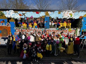 Große Gruppe verkleideter Menschen posiert vor und auf einem bunt gestalteten Karnevalswagen mit Märchenmotiven, viele halten bunte Luftballons.
