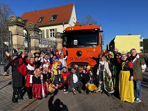 "Gruppe von kostümierten Menschen in Märchen- und Tierverkleidungen posiert vor einem orangefarbenen LKW mit der Aufschrift �SCHADE�.