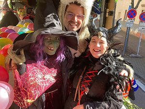 rei verkleidete Personen � eine Hexe mit grünem Gesicht und spitzem Hut, eine Person im weißen Bärenkostüm und eine als Maleficent verkleidete Frau � posieren lachend, bunte Luftballons im Hintergrund.