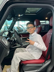 Jamil aus �The Voice Kids� sitzt auf dem Fahrersitz eines schwarzen Mercedes mit roter Lederausstattung, lächelt in die Kamera und zeigt ein Peace-Zeichen.