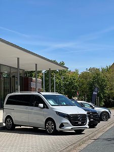 Ein weißer Mercedes-Benz Van ist vor der Stadthalle Wittenberg geparkt, dahinter ein weiteres schwarzes Fahrzeug und eine Mercedes-Fahne.