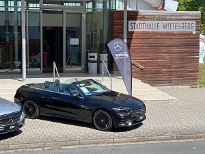 Ein schwarzes Mercedes-Benz Cabriolet steht vor der Stadthalle Wittenberg neben einer Mercedes-Fahne. Das Dach ist geöffnet, der Innenraum ist zu sehen.
