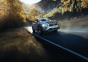 Fahrt durch die Berge: Silberner Mitsubishi Outlander f&auml;hrt dynamisch auf einer kurvigen Bergstra&szlig;e, umgeben von herbstlich gef&auml;rbten B&auml;umen.