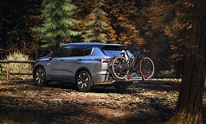 Mit Fahrradtr&auml;ger: Heckansicht des Mitsubishi Outlander mit montiertem Fahrradtr&auml;ger und zwei Fahrr&auml;dern, geparkt in einem Waldgebiet.