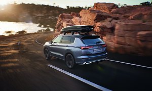 Mit Dachbox: Mitsubishi Outlander von hinten auf einer K&uuml;stenstra&szlig;e, mit montierter Dachbox, umgeben von Felsen und Blick auf das Meer.