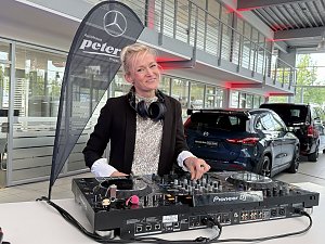 DJane mit Kopfh&ouml;rern steht an einem Pioneer-DJ-Pult in einer Mercedes-Benz Ausstellungshalle und l&auml;chelt in die Kamera.