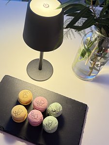 Schwarze Servierplatte mit sechs bunten Macarons, alle mit Aufdruck She�s Mercedes, daneben Tischlampe und Blumenvase.