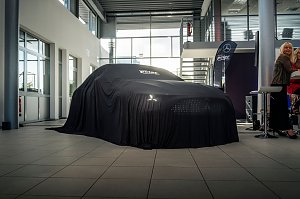  Ein Mercedes-Fahrzeug ist vollst&auml;ndig mit einem schwarzen Tuch bedeckt, auf dem Autohaus Peter steht, in einem hellen Ausstellungsraum.