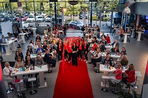 Eine gro&szlig;e Gruppe von Frauen sitzt und steht um Tische in einem Autohaus, in der Mitte posiert das She�s Mercedes-Team auf dem roten Teppich.