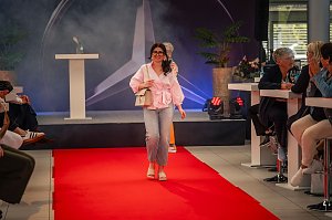 Eine junge Frau mit langen, dunklen Haaren, rosa Bluse, hellen Jeans und beiger Handtasche l&auml;uft l&auml;chelnd &uuml;ber den roten Teppich.