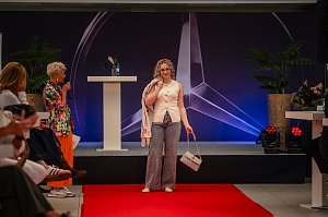Eine blonde Frau mit Brille, &auml;rmellosem cremefarbenem Oberteil, gemusterten Hosen und passender Handtasche pr&auml;sentiert sich am Ende des roten Teppichs.