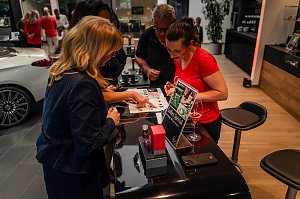 Mehrere Frauen betrachten eine Duftauswahl an einem Ladies Special-Stand, eine Frau tr&auml;gt ein rotes Shirt.eine Frau tr&auml;gt ein rotes Shirt und h&auml;lt ein Glas Ros&eacute;.